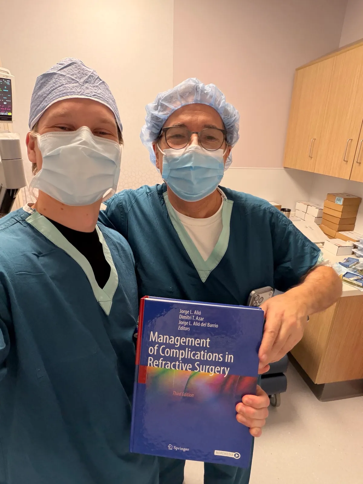 O Dr. Nicholas ao lado do Dr. Dimitri Azar no centro cirúrgico da University of Illinois Chicago, segurando o tratado de complicações em cirurgia refrativa editado por ele.